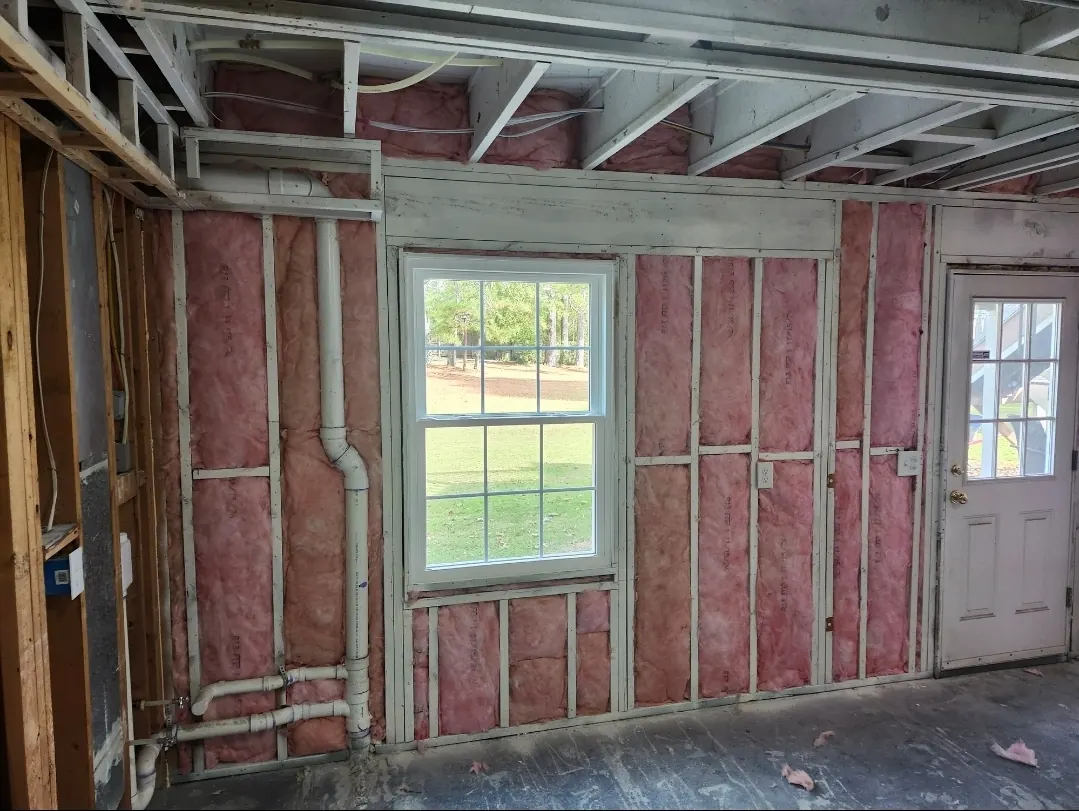 Wall insulated with pink batts fitted around plumbing, outlets and a window