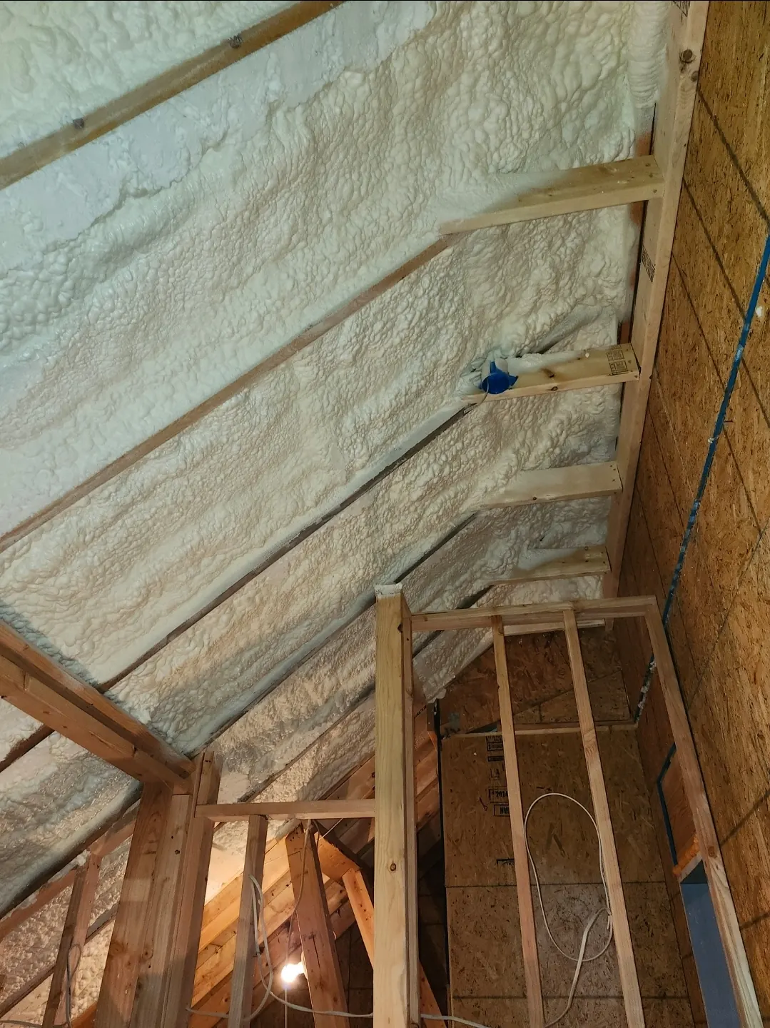 Fresh spray foam covering an attic roof deck around new wall framing